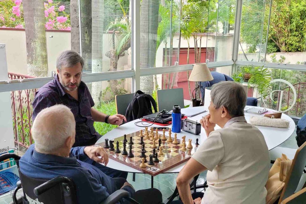 Grupo de idosos conversando e sorrindo ao redor de uma mesa em atividade de convivência".